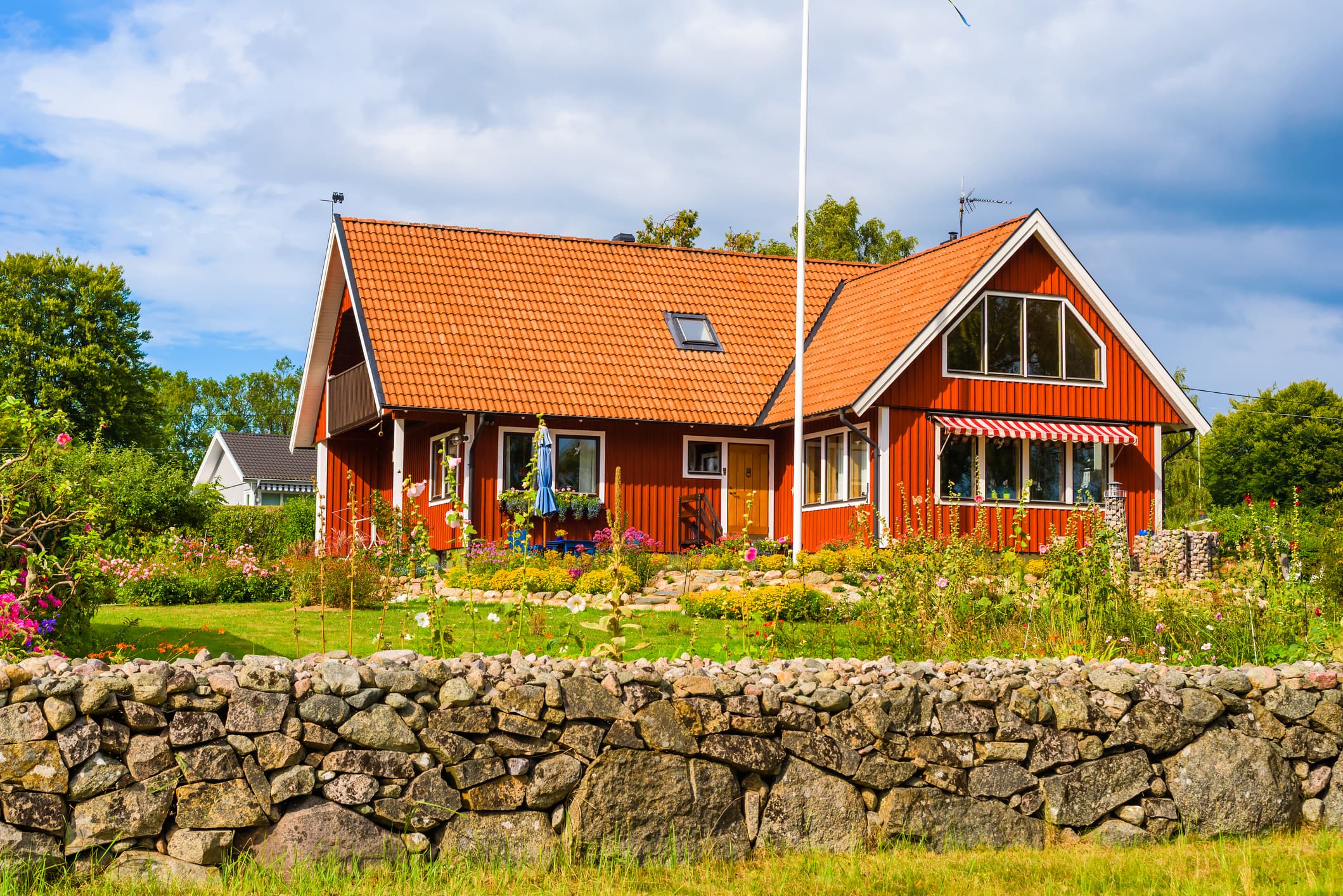 Rött svenskt trähus med blomsterträdgård och stenmur – typisk villa där mäklararvode ofta ligger högre än för lägenheter.